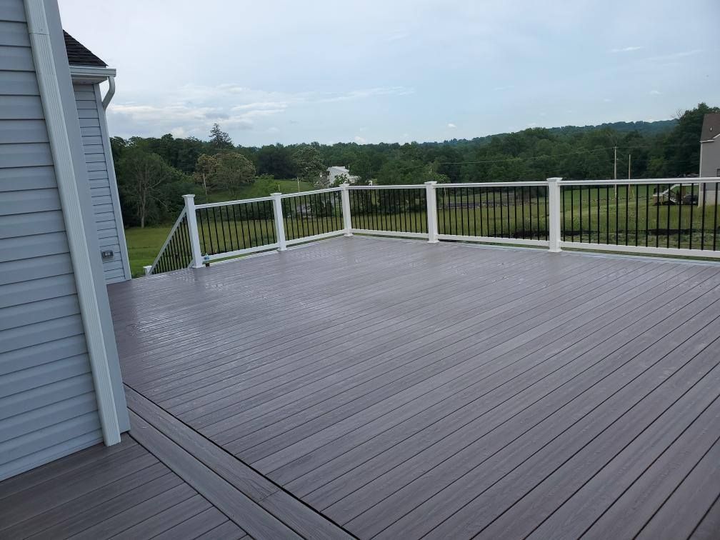 Grey composite deck with white railing and black spindles, overlooking a wooded area.