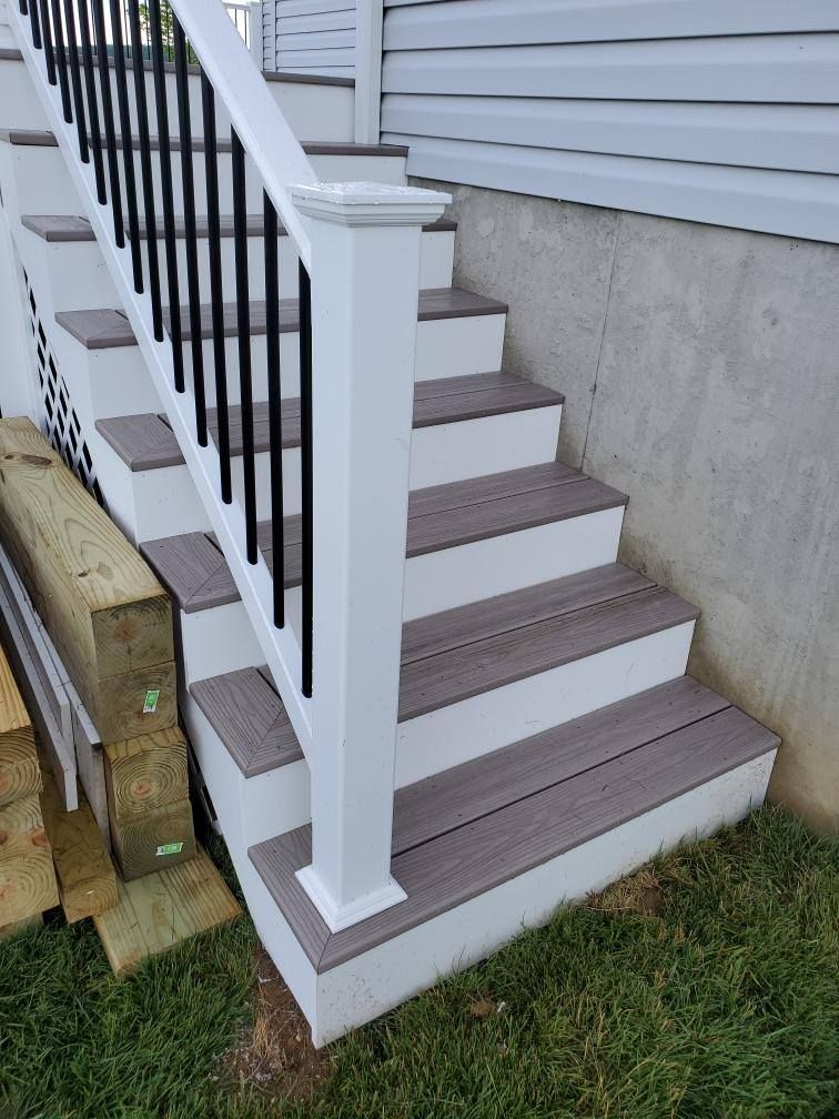 Outdoor staircase with white risers and gray treads, black railing, and white post.