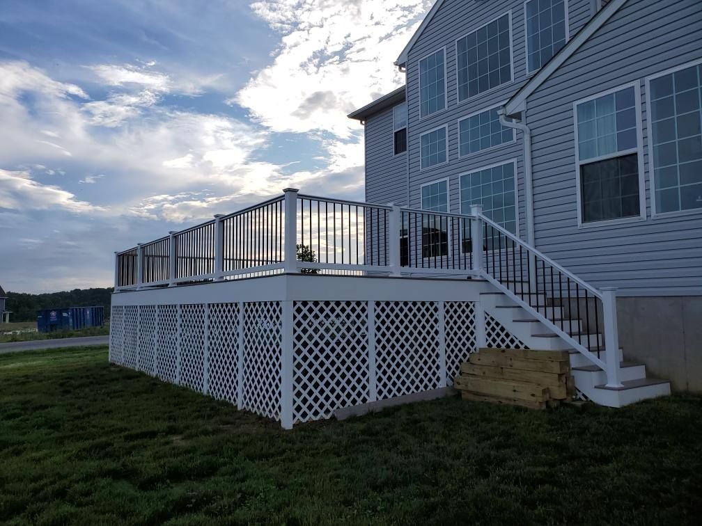 White deck with lattice, black railings, and steps leading up to a light blue house with many windows.