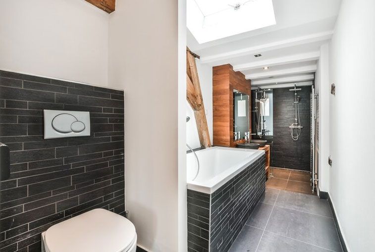 Bathroom with black brick accent wall, white toilet, tub, and shower. Skylight overhead.