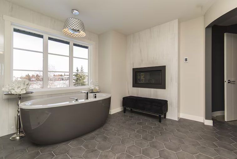 Gray soaking tub next to window in modern bathroom with fireplace.