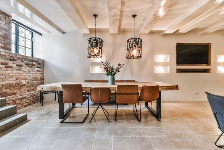 Dining room with a wooden table, brown chairs, brick wall, and hanging lamps.