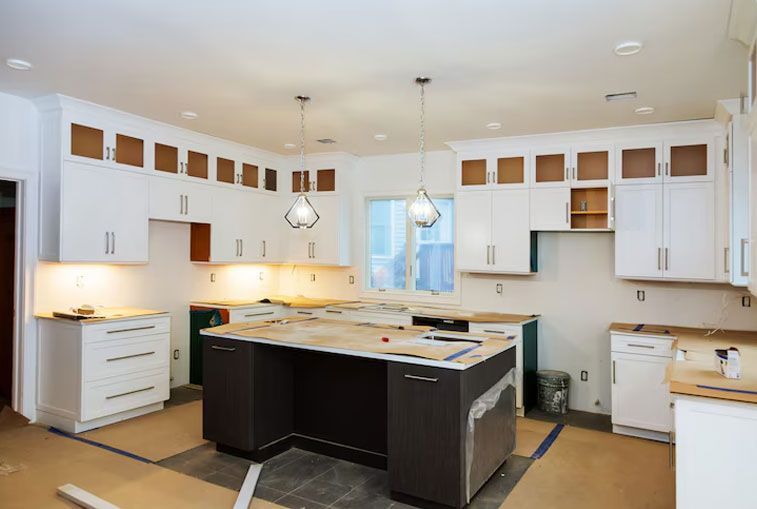 Kitchen under construction: white cabinets, dark island, exposed cabinet frames.