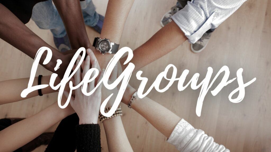 A group of people are putting their hands together in a circle for life groups.
