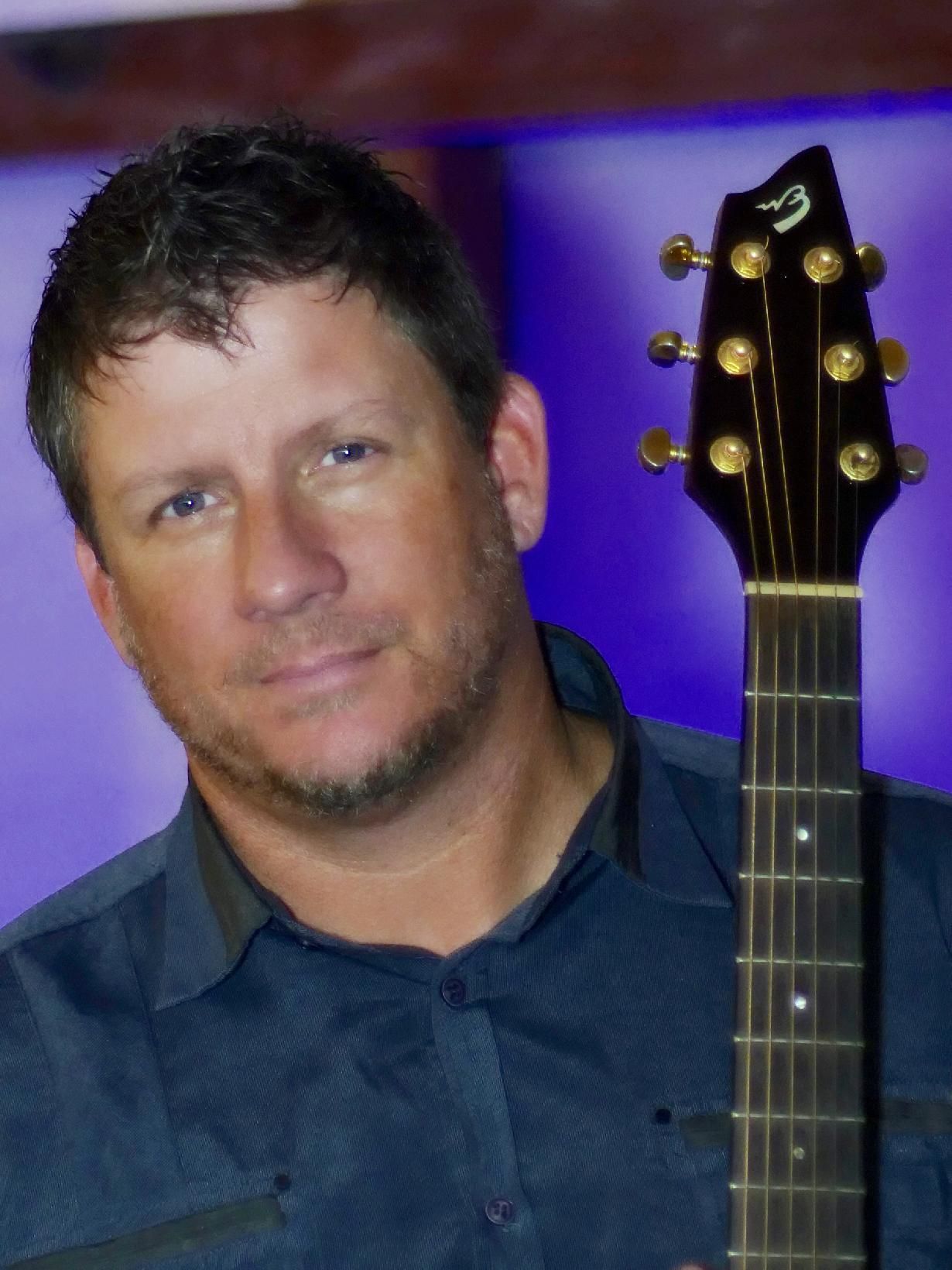 A man is holding an acoustic guitar posing for the camera