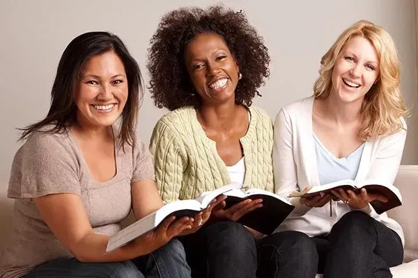 Three women are looking at a magazine together and smiling.