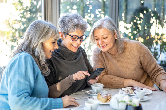 Three women are sitting next to each other on a wall and talking.