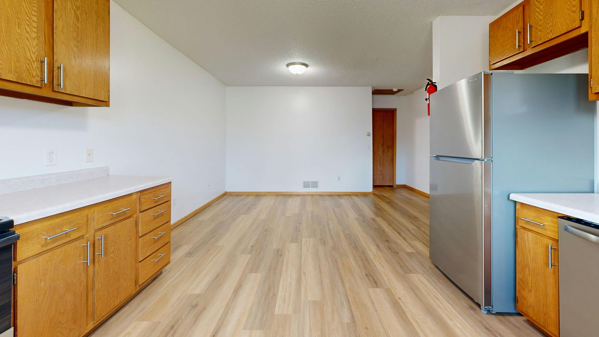 Kitchen with wooden cabinets, stainless steel refrigerator, white countertops, and wood-look flooring.