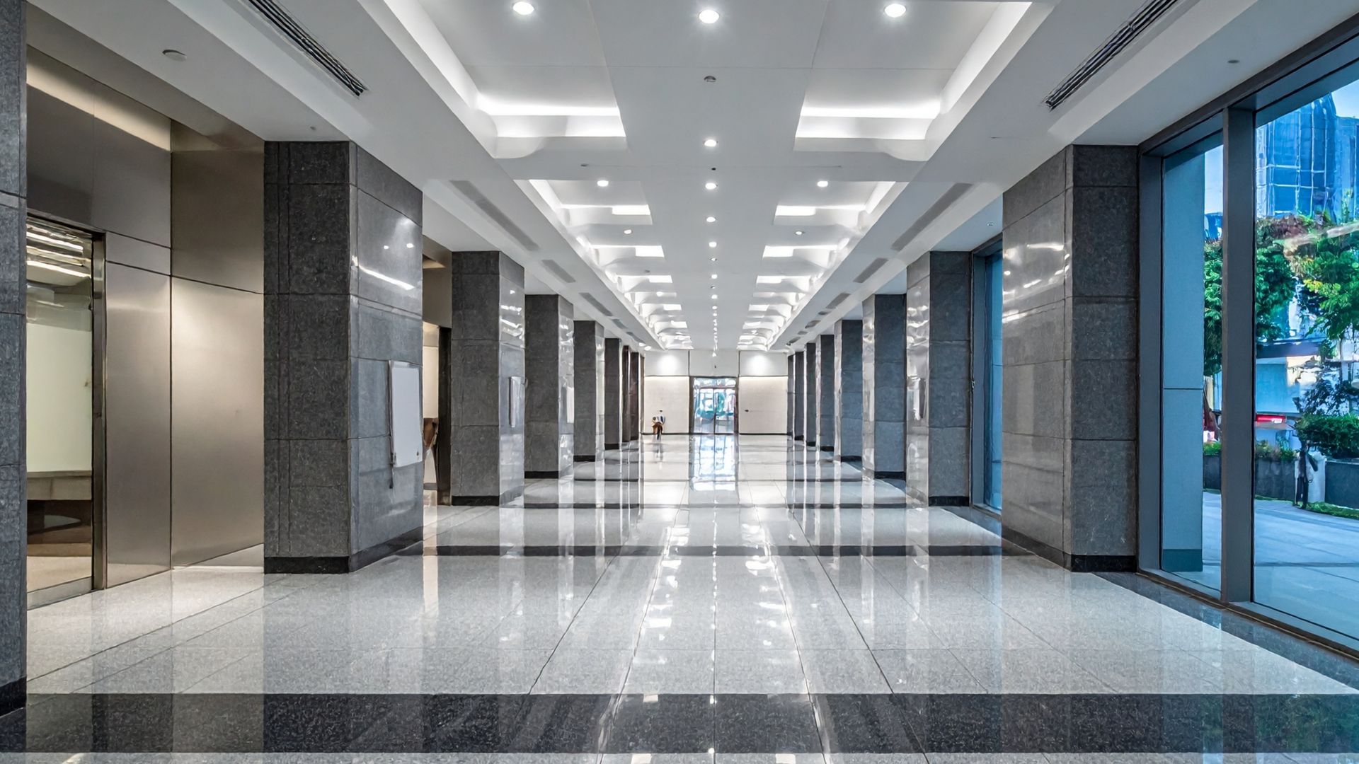 A long, modern hallway with marble floors, columns, and large windows.