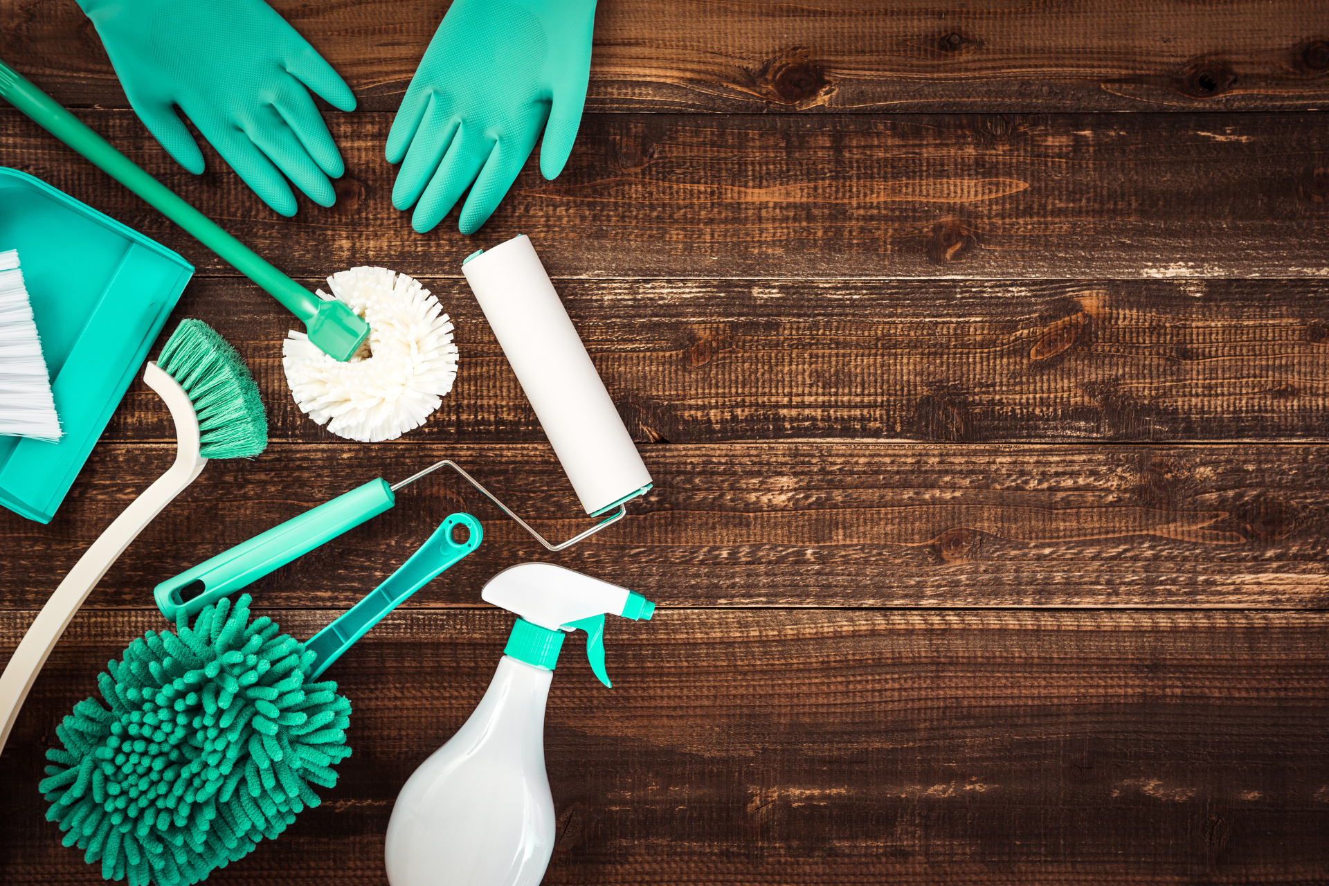 Cleaning supplies on a wooden surface: gloves, spray bottle, brushes, and a paint roller.