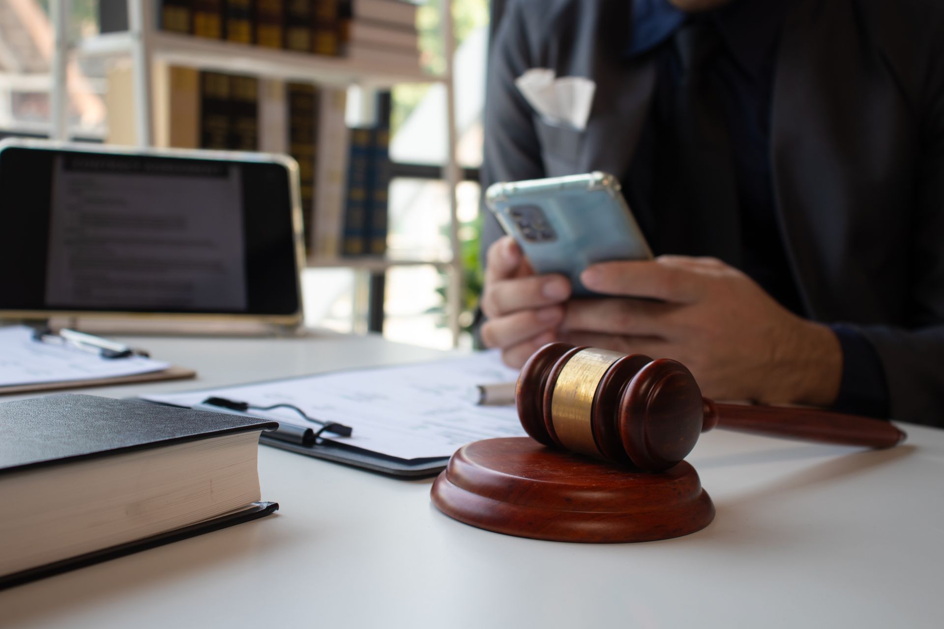 Gavel on desk in front of person using a phone and computer. Legal documents present.