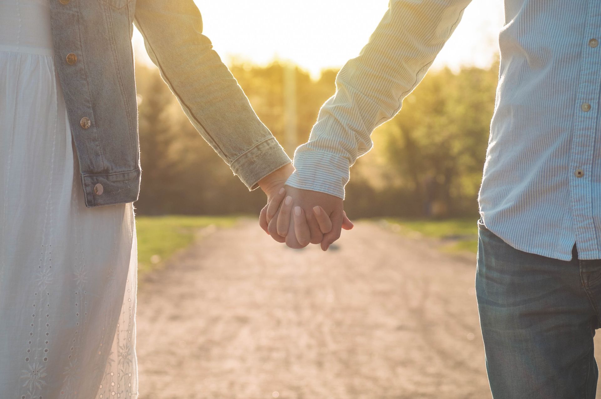 Two people holding hands while walking along a dirt path during a sunset.