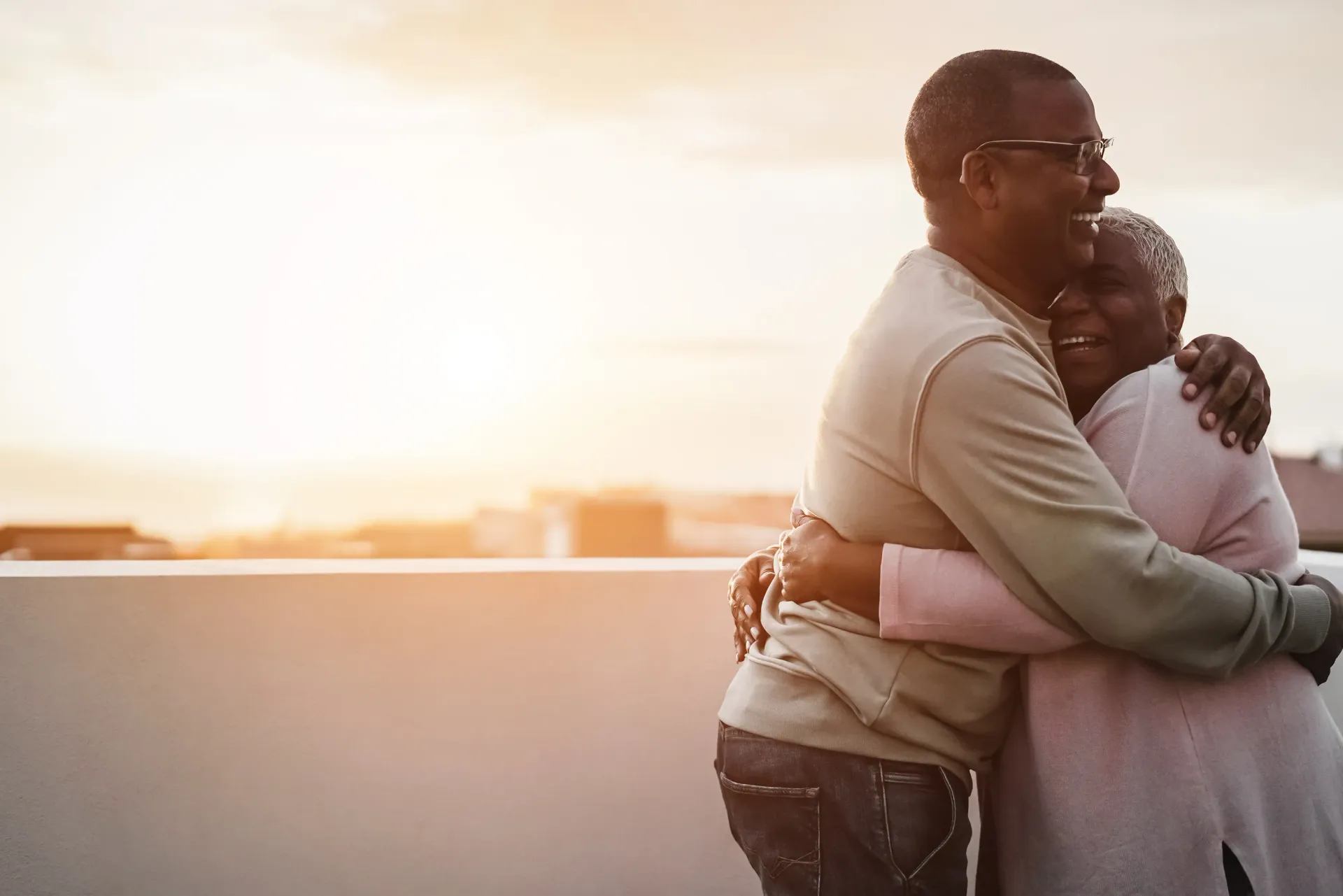 Couple embraces on a rooftop at sunset, both smiling.