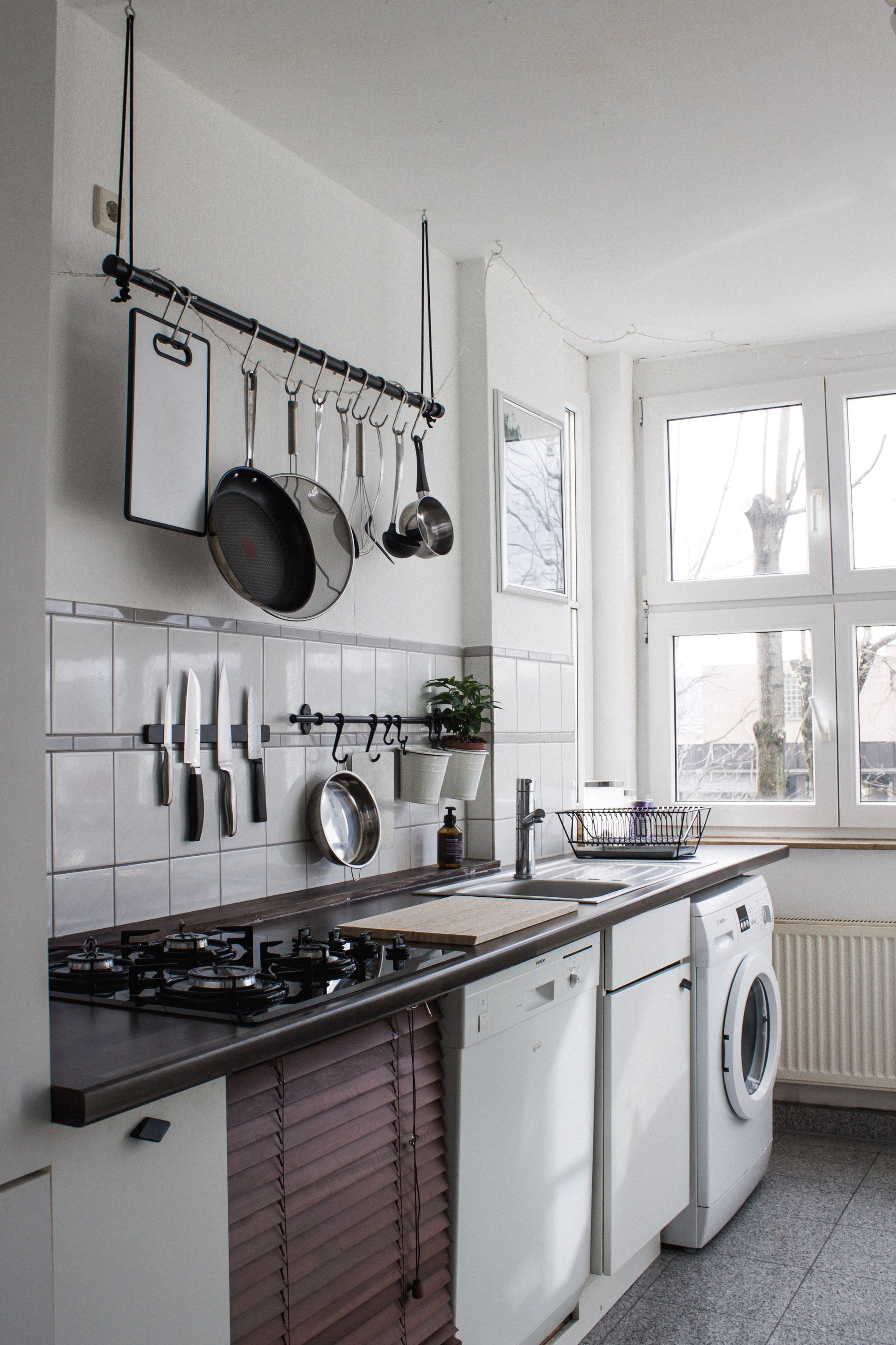 compact galley kitchen with single sink and backsplash tiling with hanging kitchen pots and pans