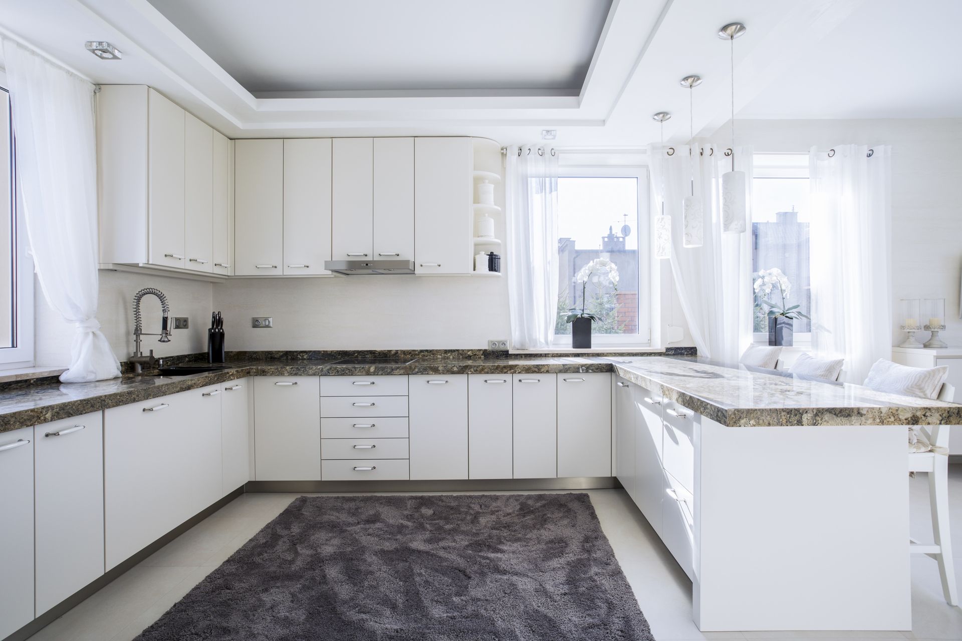 a kitchen with white cabinets and marble counter tops