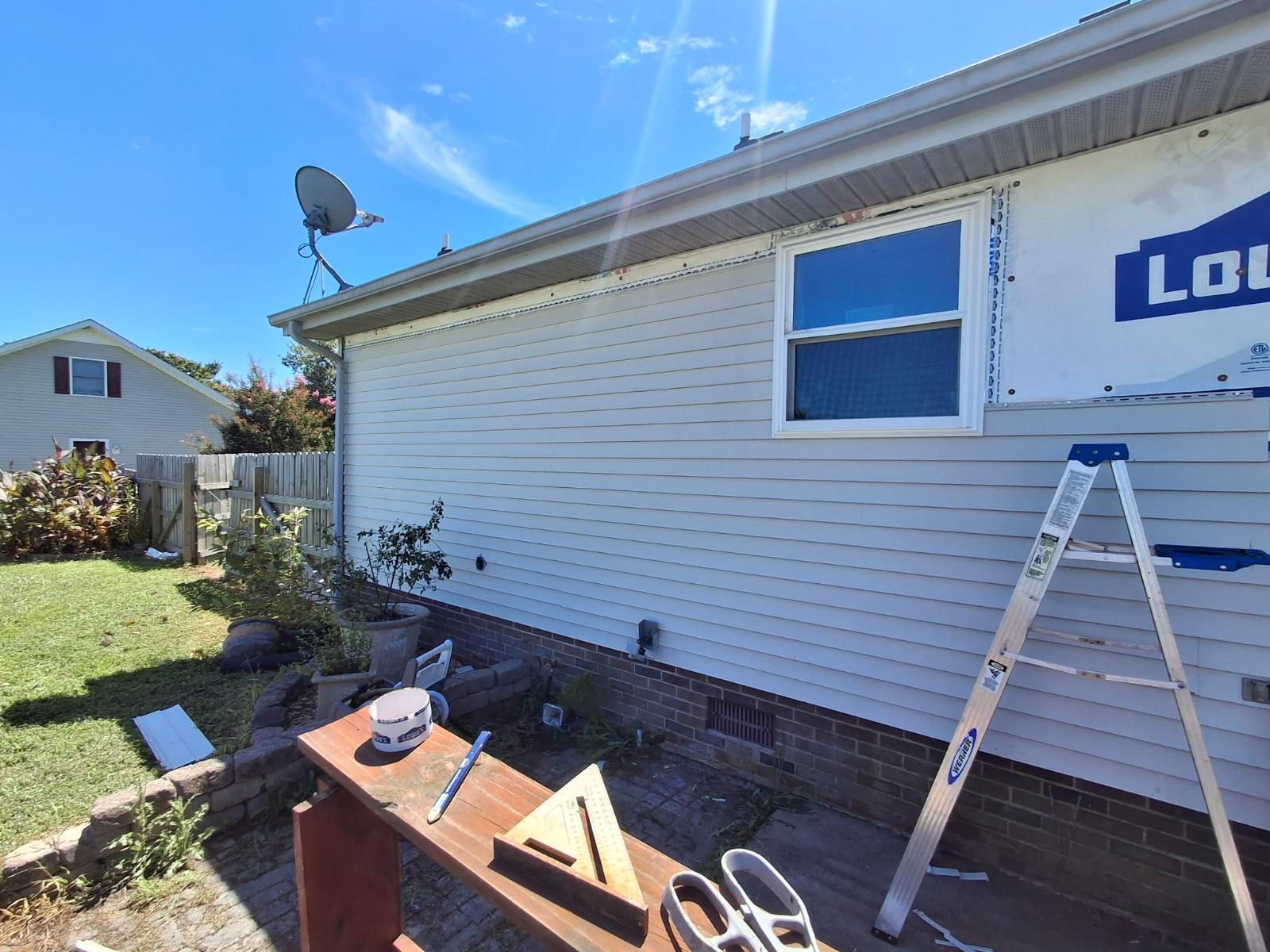 House exterior with window being installed, a ladder, and tools on a workbench.