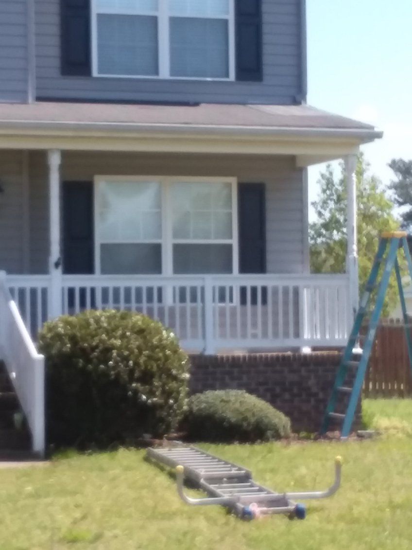 Two-story house with white porch and railing, blue shutters, and a ladder on the lawn.