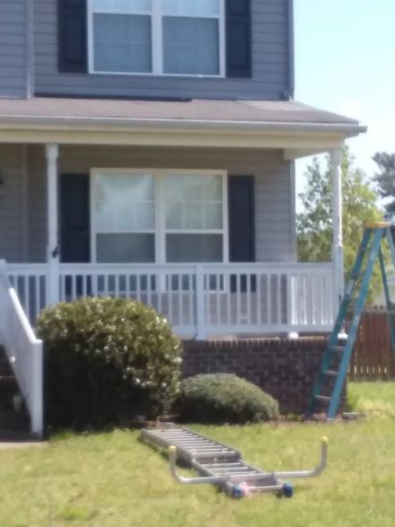 Two-story house with porch, white railing, and blue shutters. Ladder leans against the house, in grassy yard.