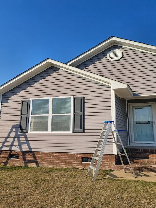 House exterior with grey siding, black shutters, brick base, and a ladder.