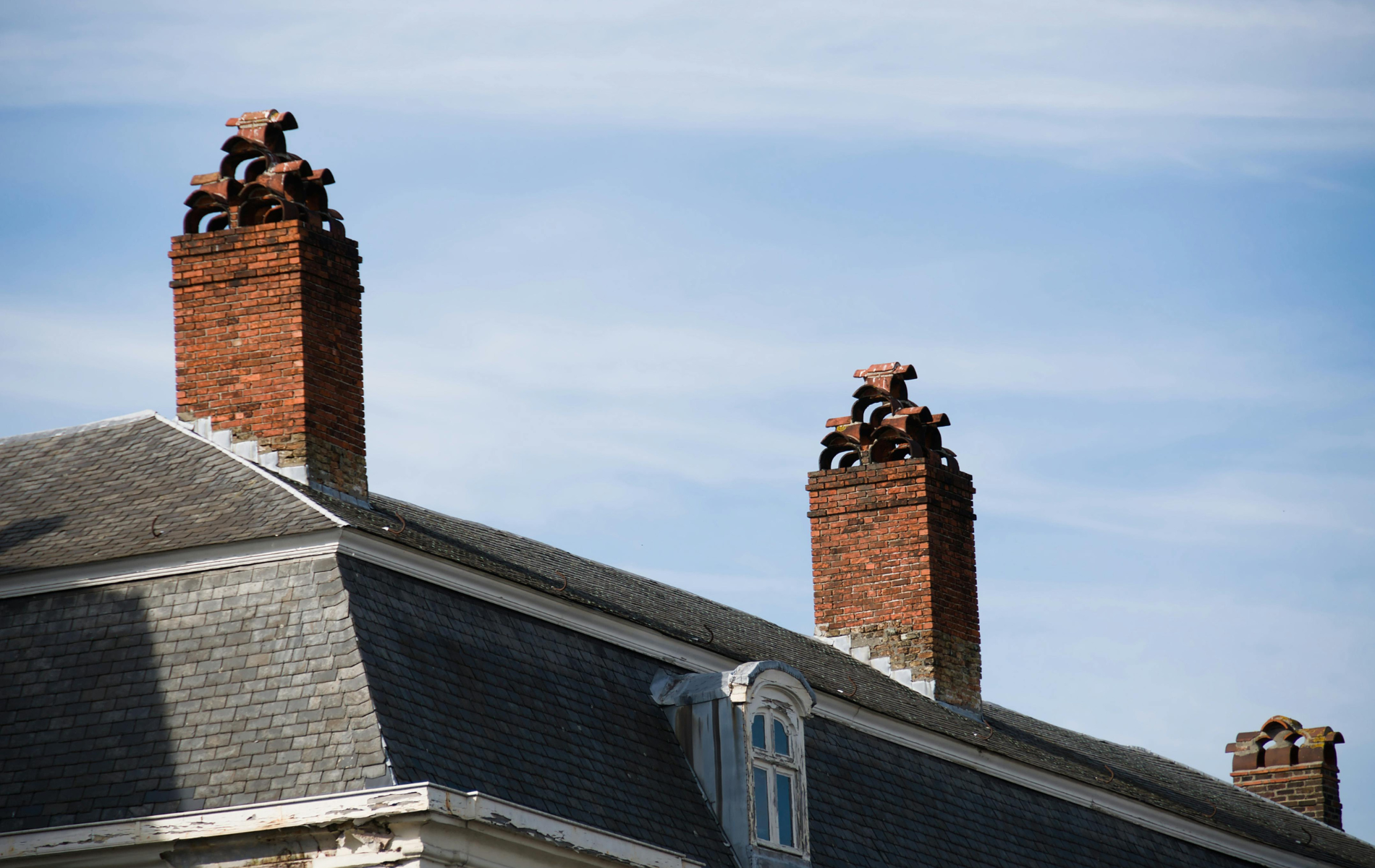 Red brick chimneys with horse sculptures atop, set against a blue sky, on a gray roof.