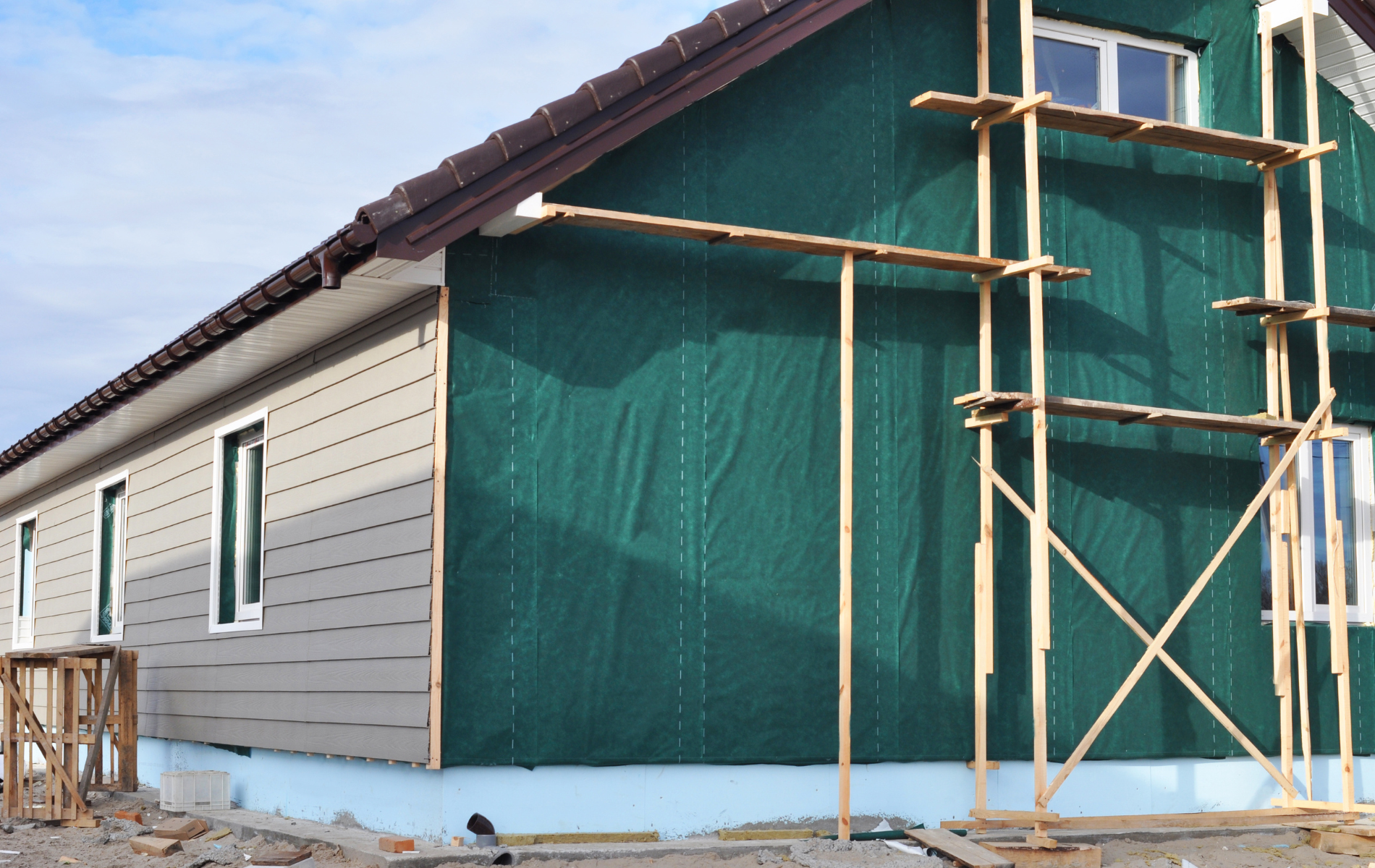 House exterior under construction, featuring green sheathing and scaffolding.