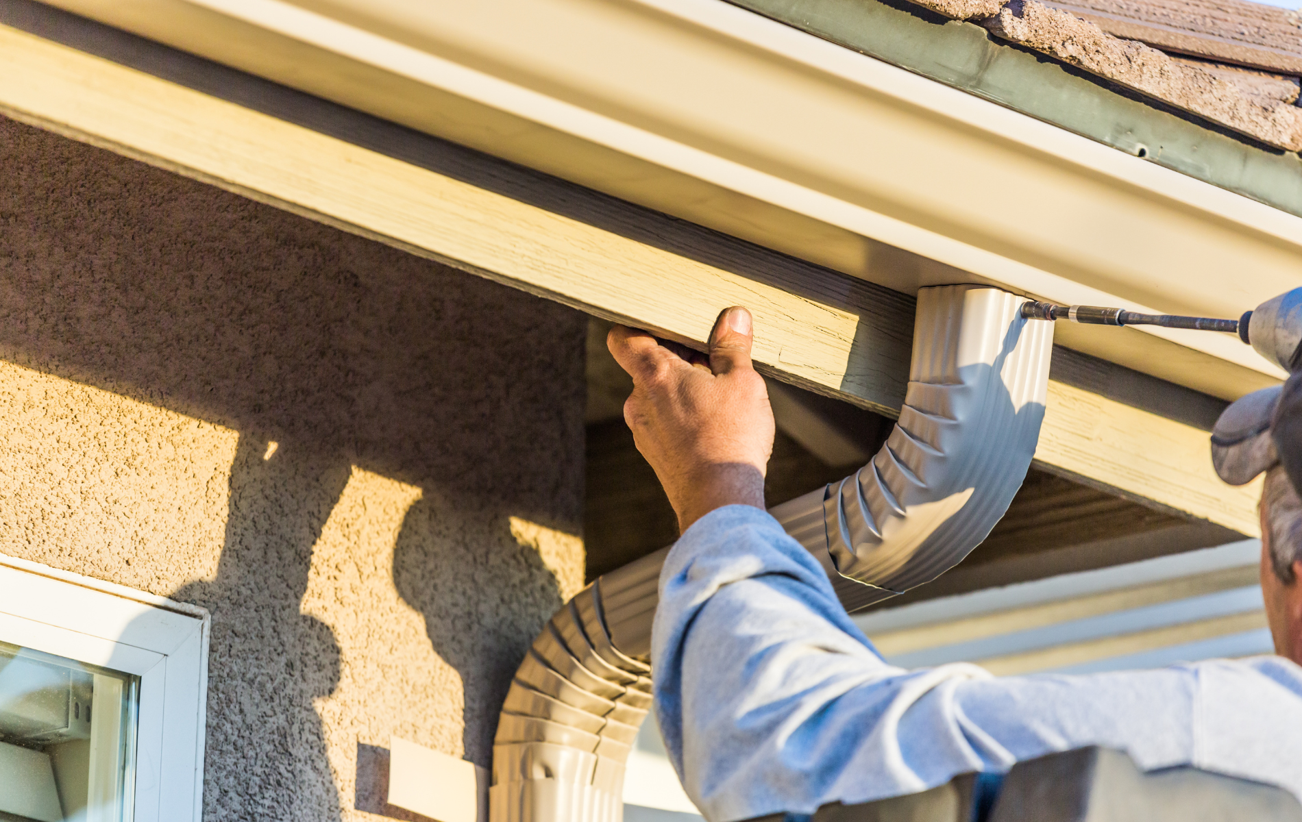 Person installing a gutter with a power drill on a house.