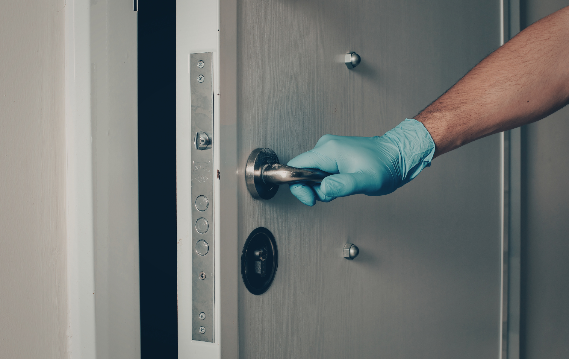 Person wearing blue glove opening a gray door with a silver handle.