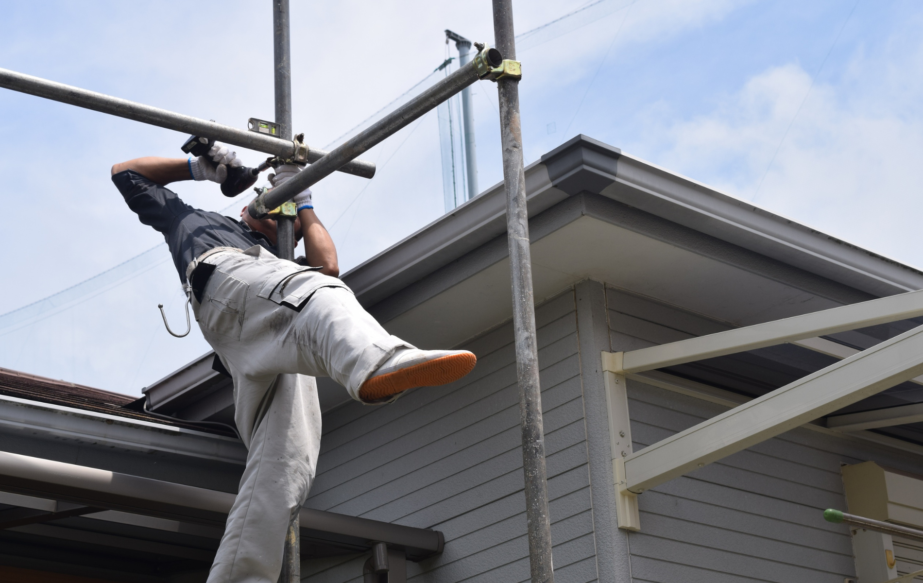 Construction worker on scaffolding, working near a house's roof edge on a sunny day.