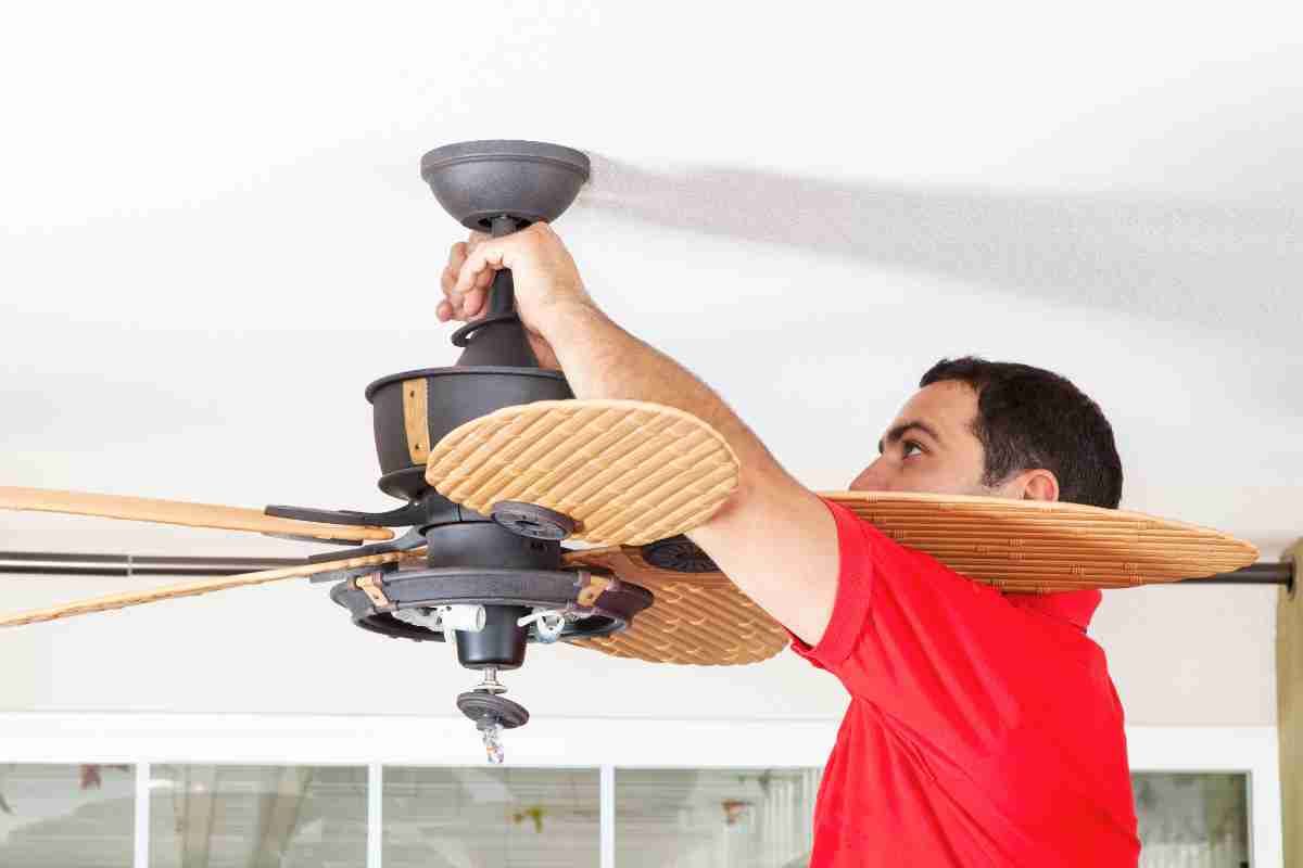 Man in red shirt installing a ceiling fan on a white ceiling.
