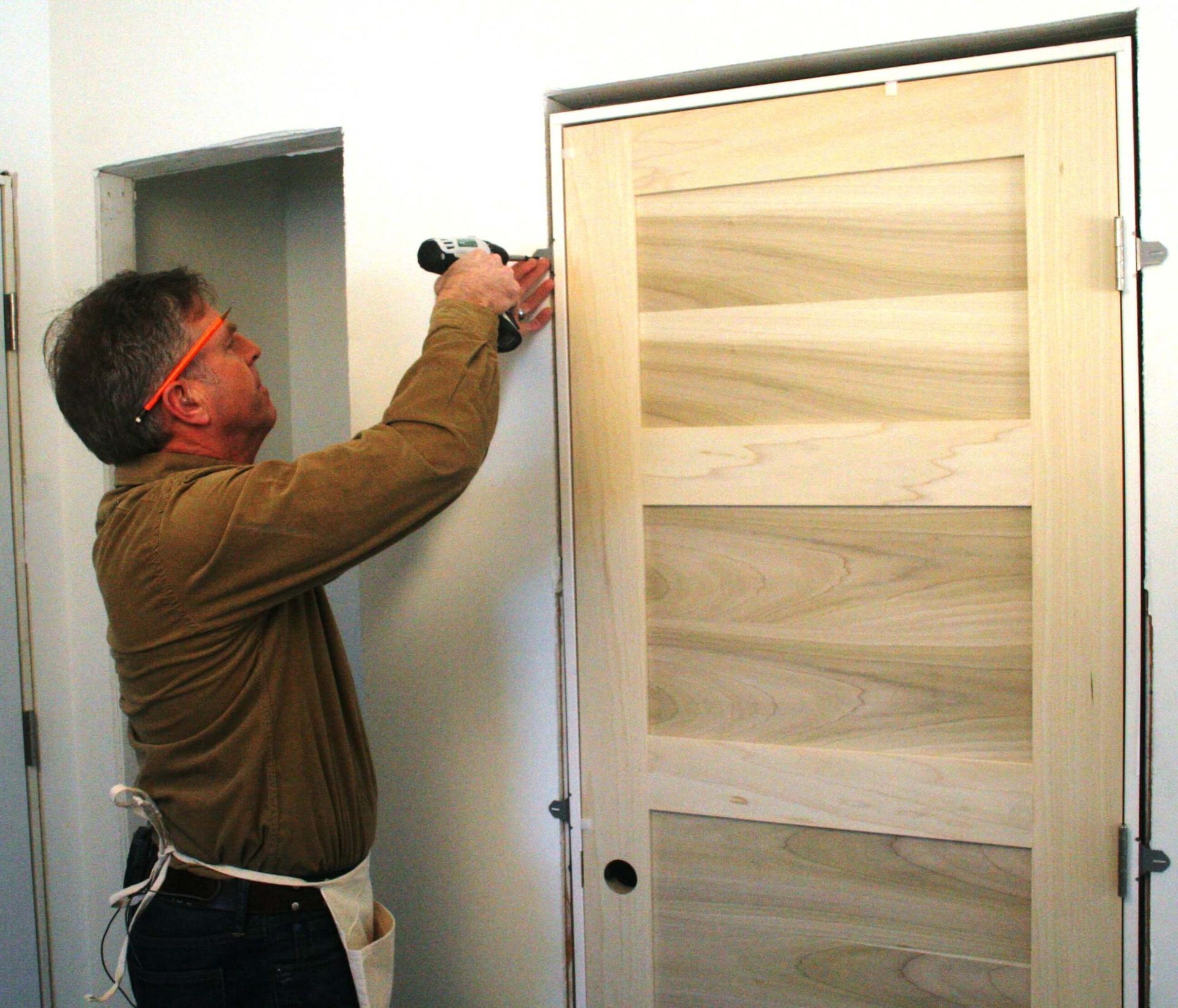 Man with safety glasses using a power drill to install a door frame.