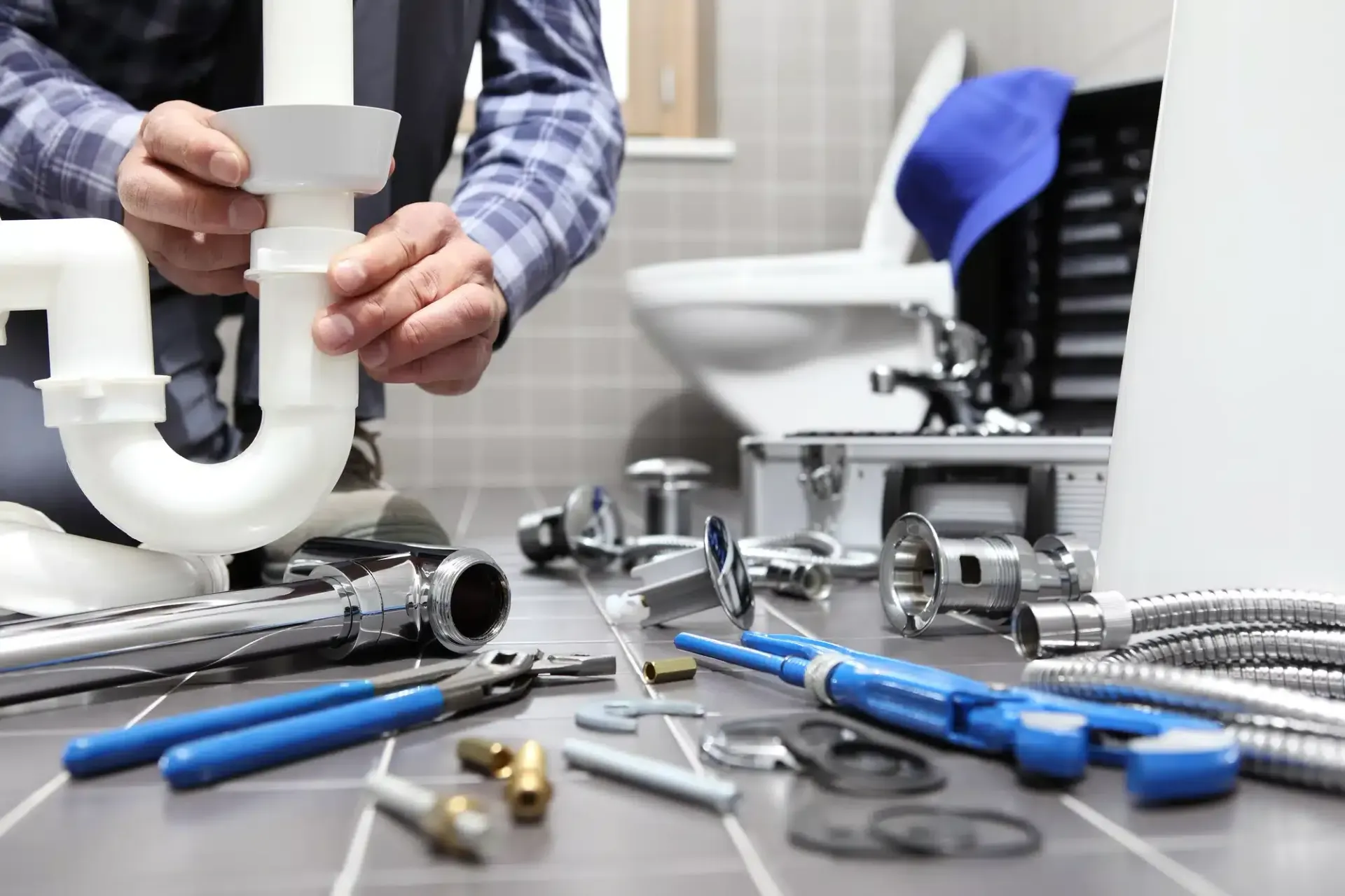 Plumber in bathroom fixing pipes, surrounded by tools on floor near toilet.
