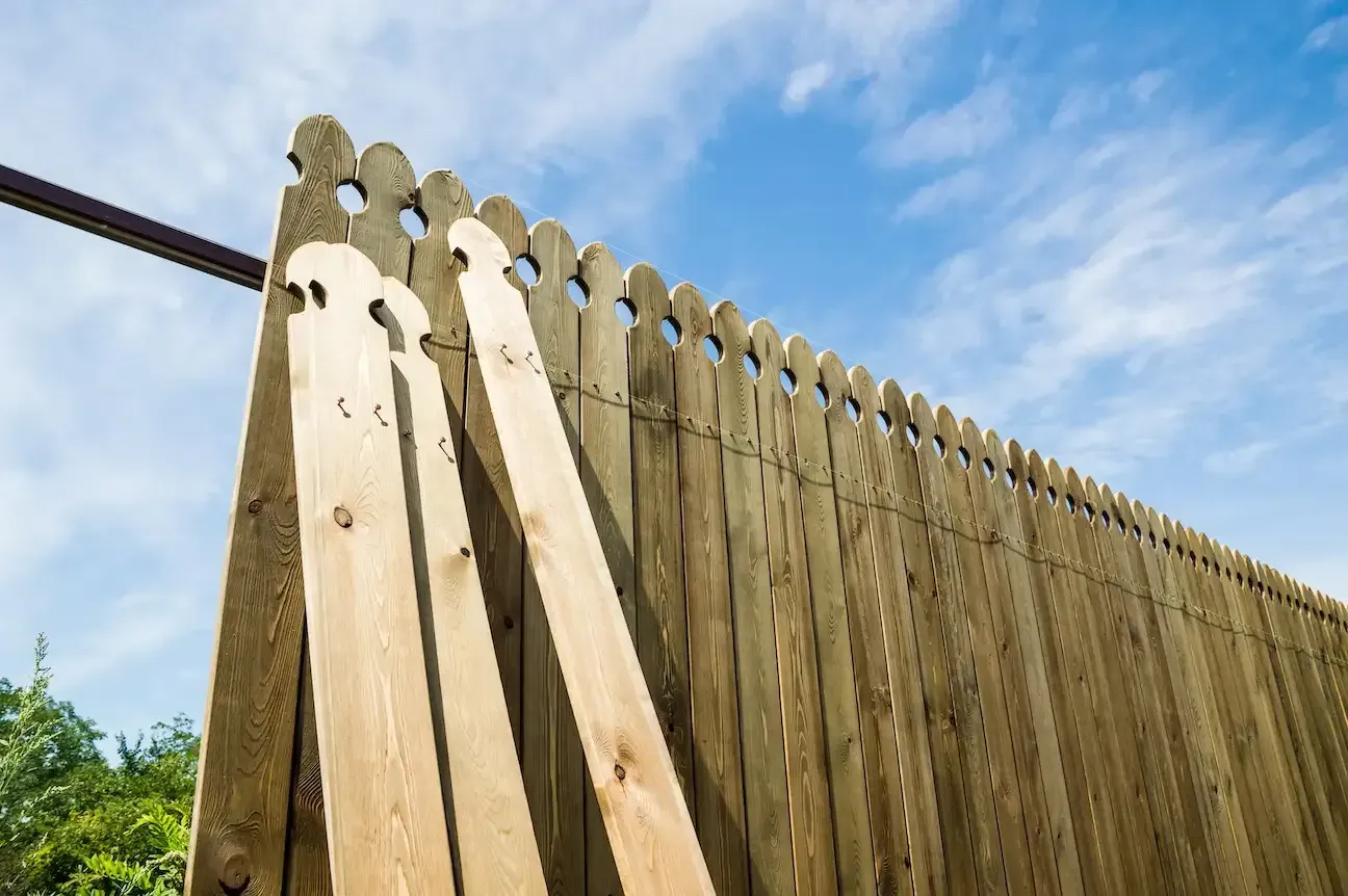 Wooden fence with decorative top against a blue sky with scattered clouds.