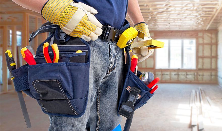 Construction worker wearing a tool belt, inside a room under construction, holding tools.