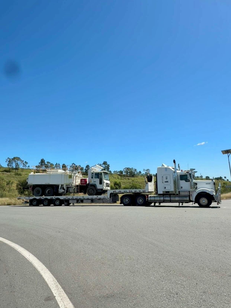 Two utility trucks parked on a roadside under a clear blue sky, one carrying a tracked machine.— Full Torque Transport In Parkhurst, QLD 