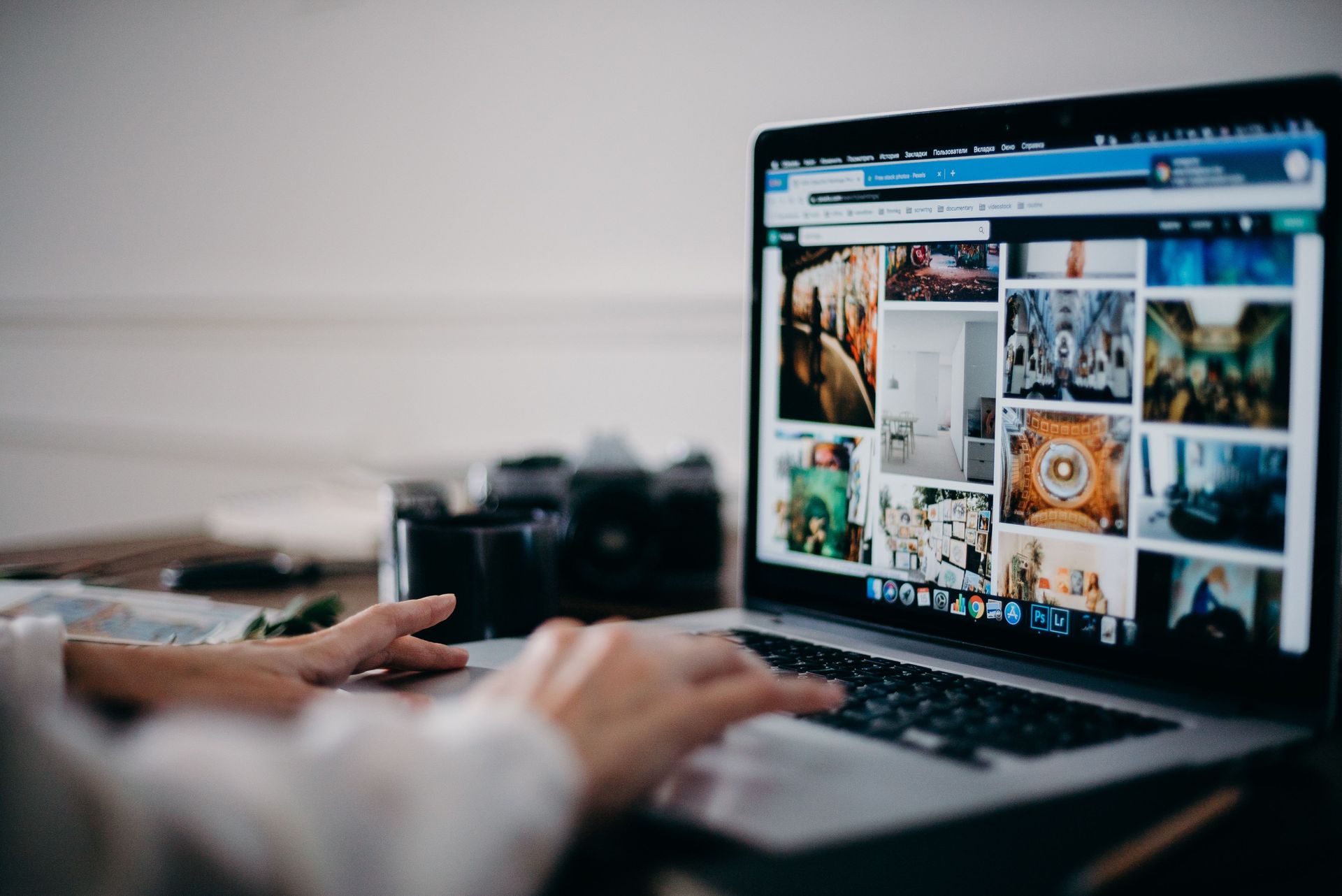 Hands typing on a laptop displaying a photo gallery, with a camera beside it on a desk.