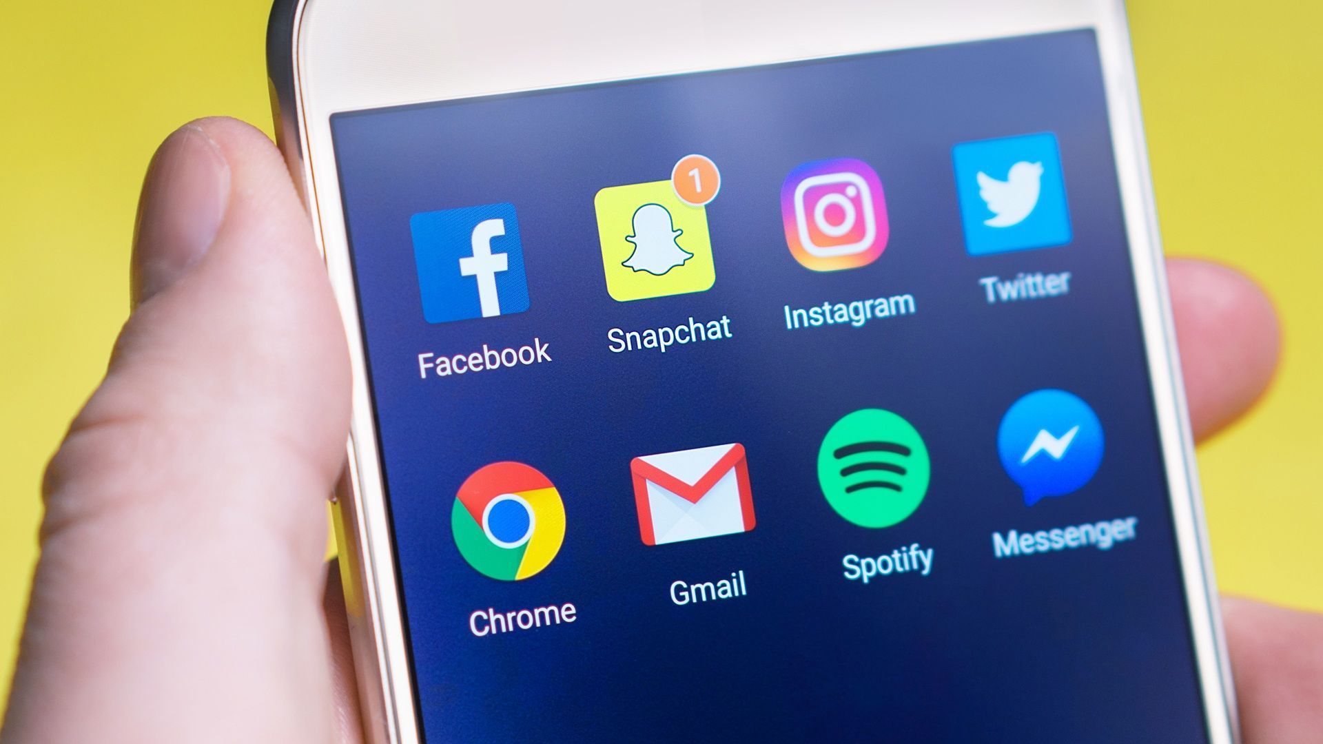 Hand holding a smartphone displaying social media and app icons on a blue screen