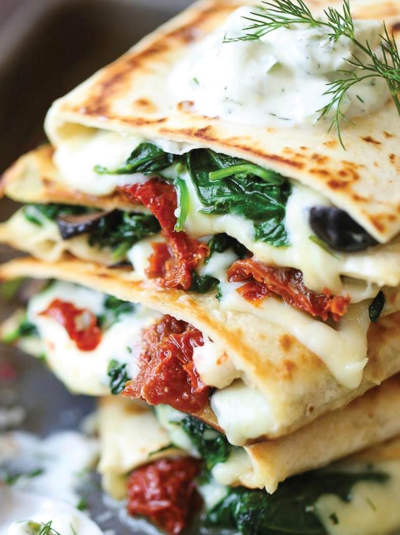 A close up of a stack of quesadillas with spinach , cheese and sun dried tomatoes.