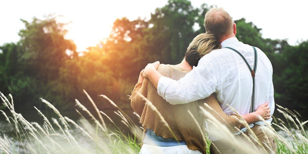 A man and a woman are standing in a field hugging each other.