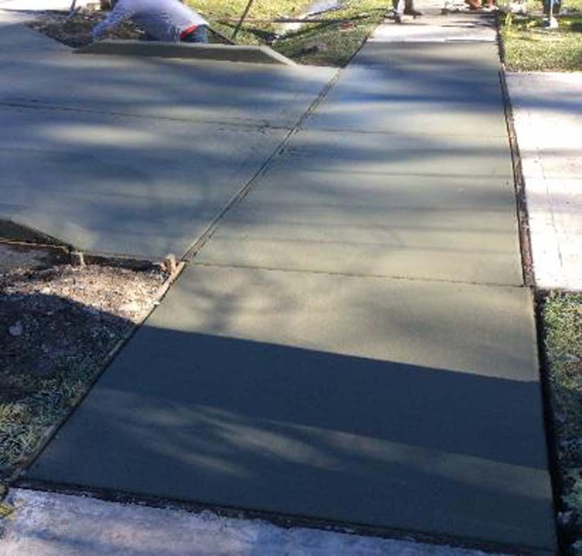 A man is laying concrete on a sidewalk.