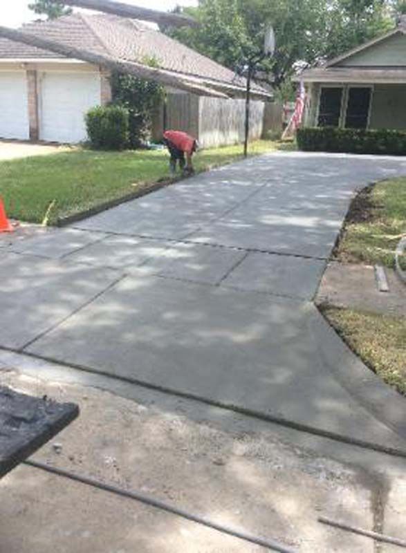 A man is working on a concrete driveway in front of a house.