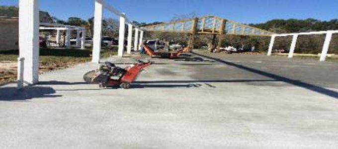 A concrete saw is cutting a concrete driveway in a parking lot.