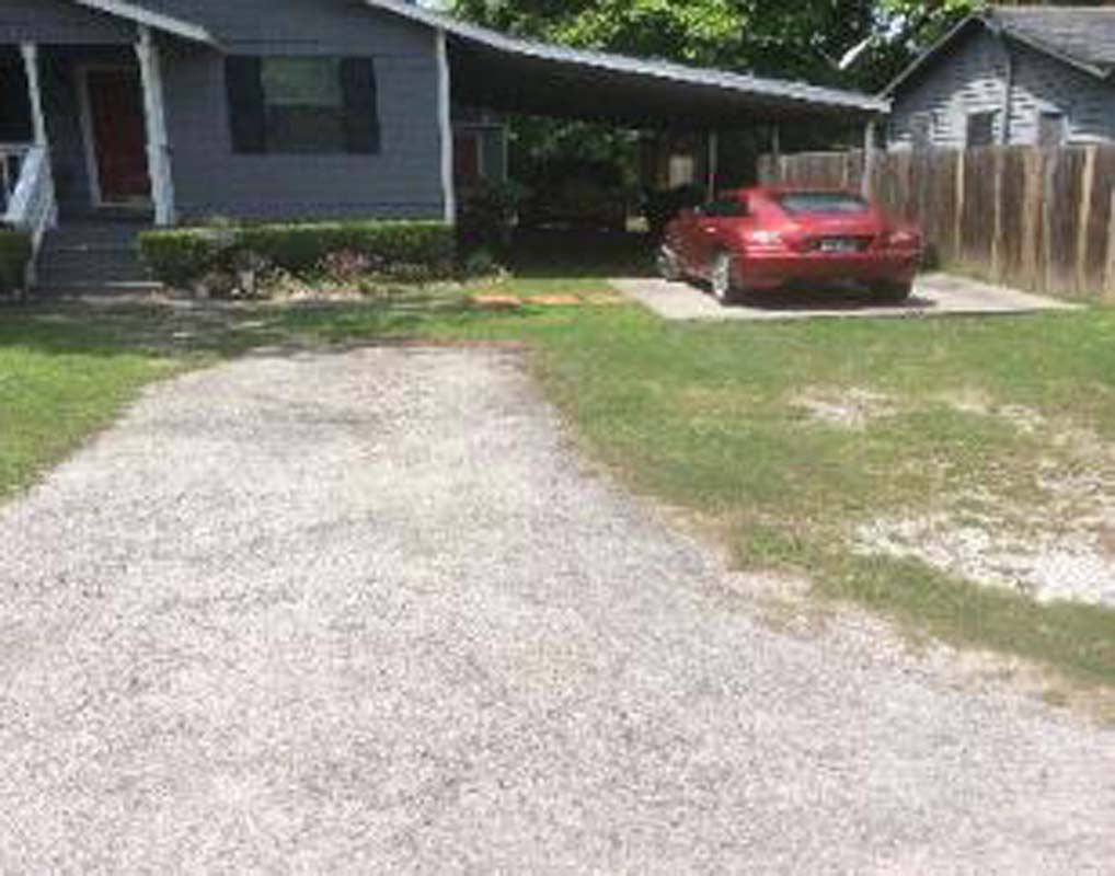 A red car is parked under a carport in front of a house.