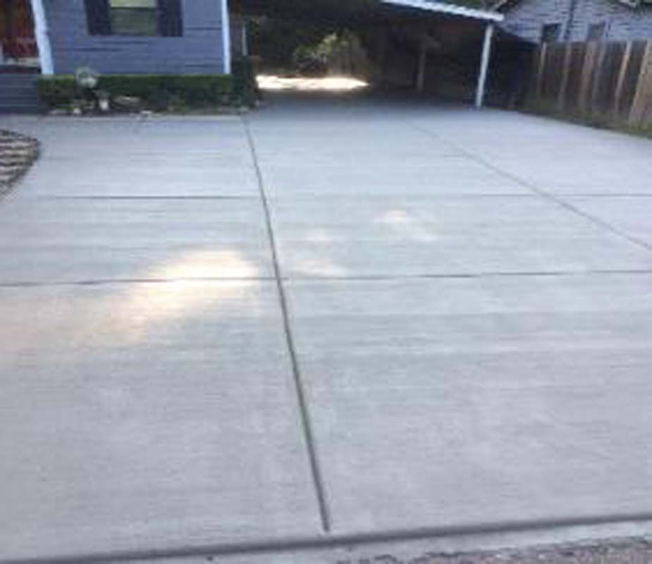 A concrete driveway leading to a house with a carport.