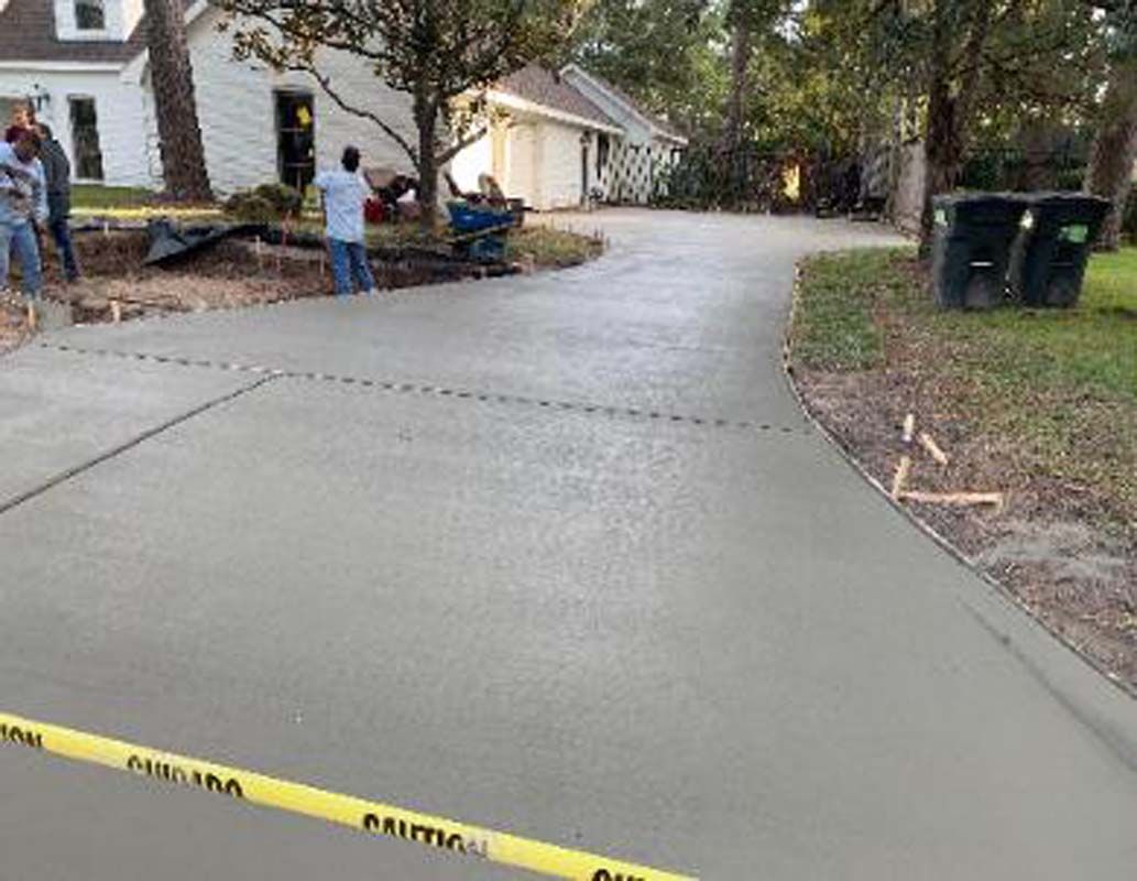 A group of men are working on a concrete driveway in front of a house.