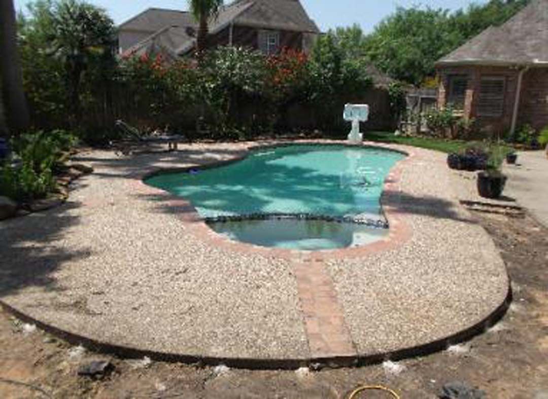 A large swimming pool is surrounded by a concrete patio in a backyard.