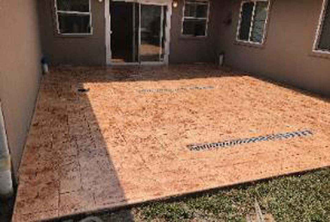 A large concrete patio with a sliding glass door in the backyard of a house.