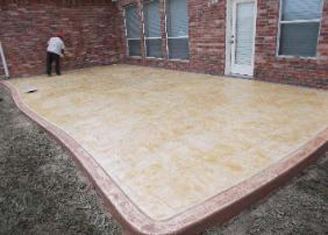 A man is standing on a concrete patio in front of a brick house.