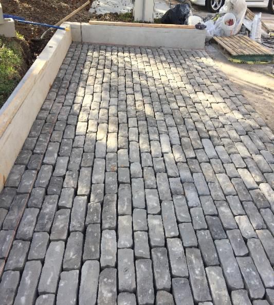 A brick driveway with a white border and a car parked in the background