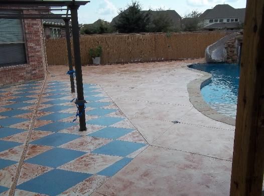 A patio with a checkered pattern and a pool in the background
