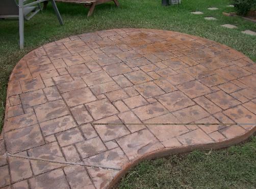 A concrete patio with a brick pattern is sitting on top of a lush green lawn.